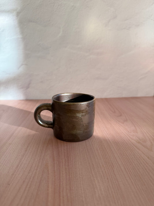 Handmade ceramic mug in a glossy bronze metallic glaze on a wood table